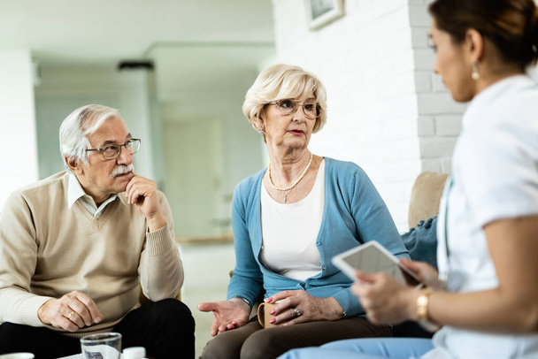 Senior couple and healthcare worker communicating during home visit.  - Photo, Image