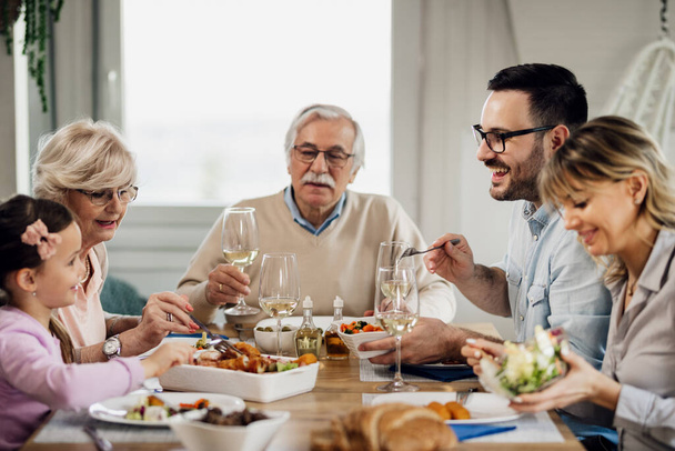 Happy multi-generation family eating lunch at dining table. Focus is on mid adult man talking to his daughter.  - 写真・画像