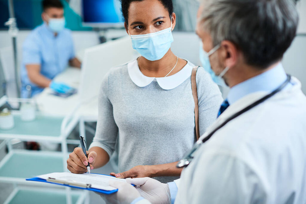 Чорна жінка розмовляє зі своїм стоматологом під час підписання документа в стоматологічній клініці під час пандемії коронавірусу
. - Фото, зображення