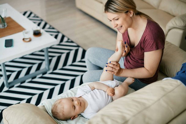 Cute baby boy lying down on sofa while mother is massaging his leg at home. - Fotografie, Obrázek