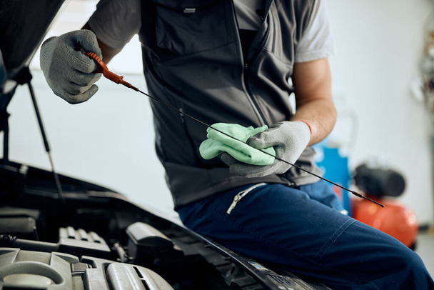 Araba atölyesinde çalışırken yağ manivelasını kontrol eden tanınamayan oto tamircisi.  - Fotoğraf, Görsel