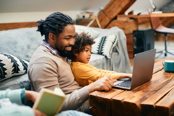African American little girl and her father using computer while relaxing at home. - 写真・画像