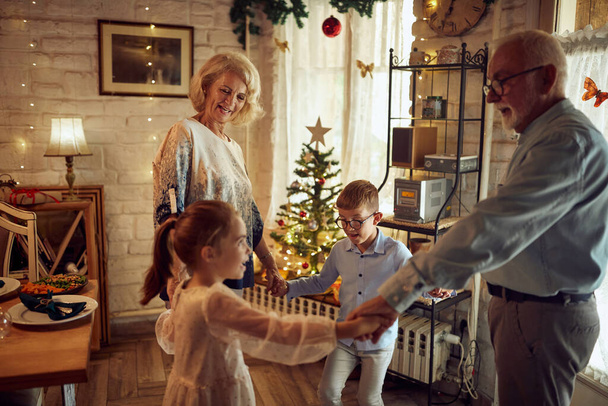 Happy senior couple holding hands with their grandchildren while playing  playing ring around the rosy on Christmas at home. - Foto, Imagen