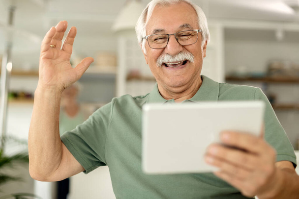 Happy mature man using digital tablet and making video call at home.  - Foto, afbeelding