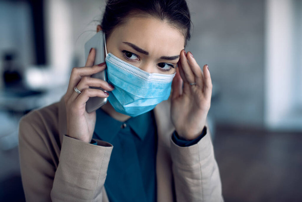Distraught businesswoman talking over cell phone while working in the office during COID-19 pandemic. - Photo, Image
