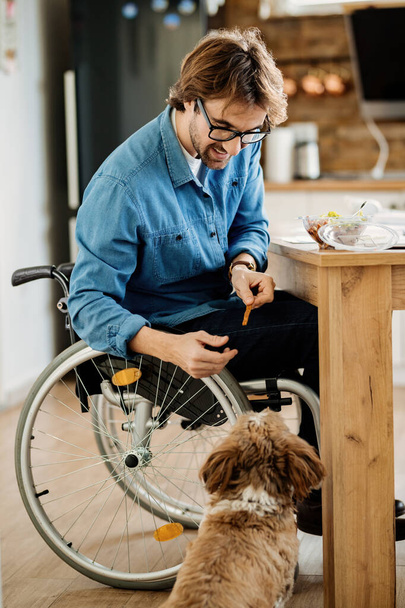 Young smiling disabled man feeding his dog while having a meal at home.  - 写真・画像