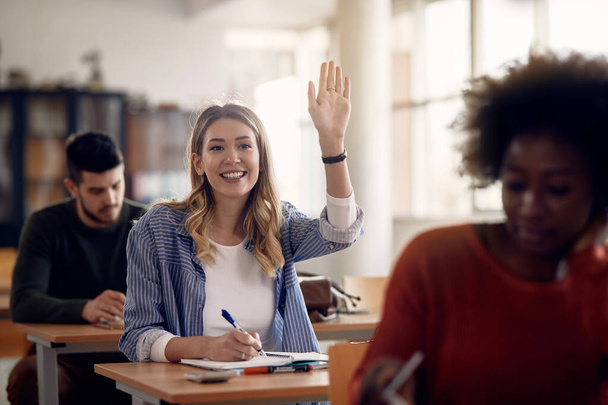 Щаслива студентка, яка піднімає руку, щоб відповісти на питання під час занять в університетському класі
.  - Фото, зображення