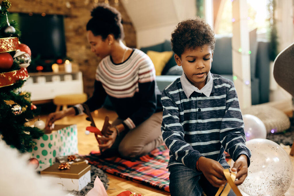 Little African American boy decorating with his mother while preparing for Christmas holiday at home. - 写真・画像