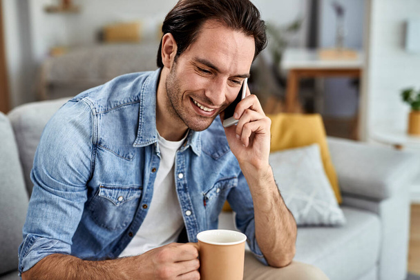 Young happy man talking on mobile phone while drinking coffee at home.  - Foto, immagini