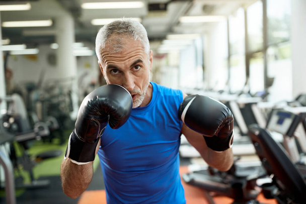 Middle aged athlete practicing boxing while working out in a gym and looking at camera.  - Φωτογραφία, εικόνα