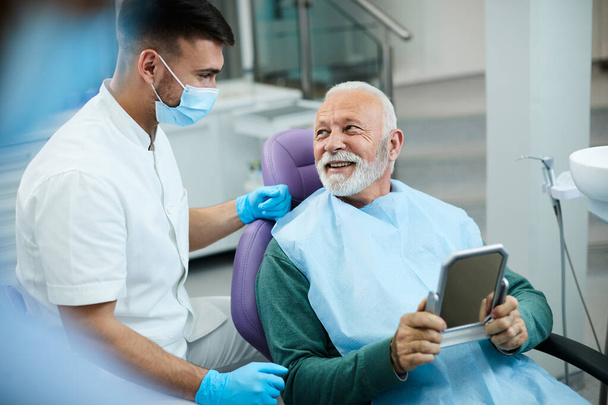 Happy senior man talking to his dentist while being satisfied with dental procedure at dentist's office. - 写真・画像