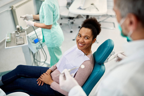 Щаслива чорна жінка розмовляє зі своїм стоматологом під час стоматологічного огляду в кабінеті стоматолога
. - Фото, зображення