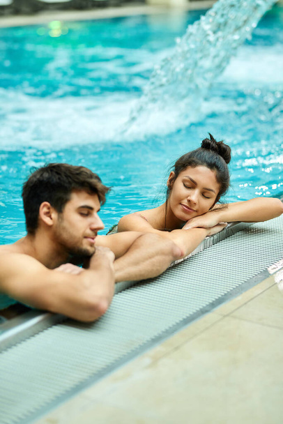 Relaxed couple leaning at the edge of a swimming pool and enjoying in the water with eyes closed at the spa.  - Photo, image