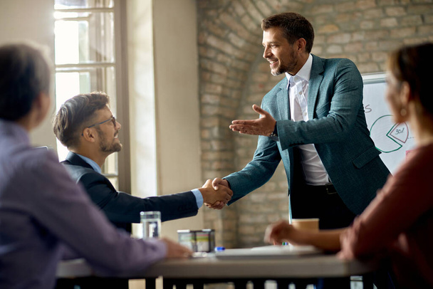 Happy businessman shaking hands with one of his coworkers while joining a meeting in the office.  - Photo, image