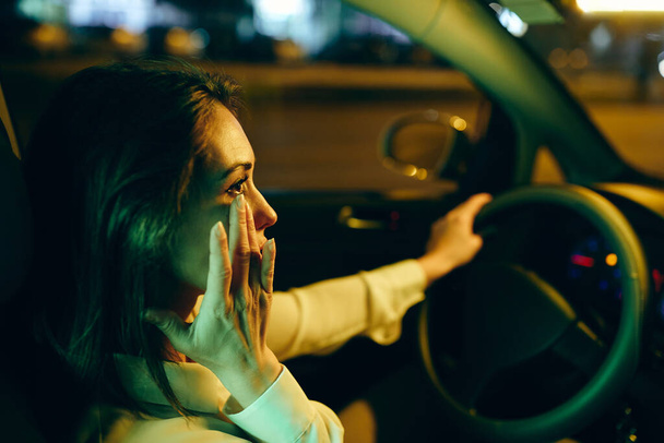 Young crying woman driving car at night and wipes away her tears.  - Foto, immagini