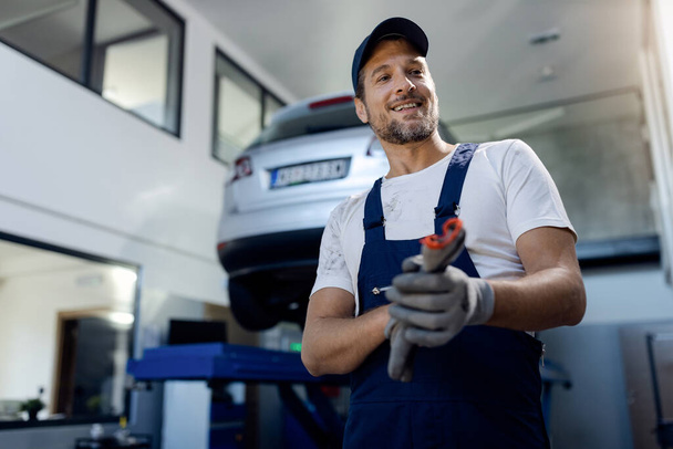 Low angle view of of happy mechanic working at auto repair shop. - Φωτογραφία, εικόνα