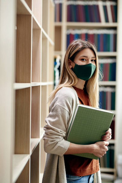 Portrait of college student wearing protective face mask while learning in library during coronavirus pandemic. - Foto, immagini
