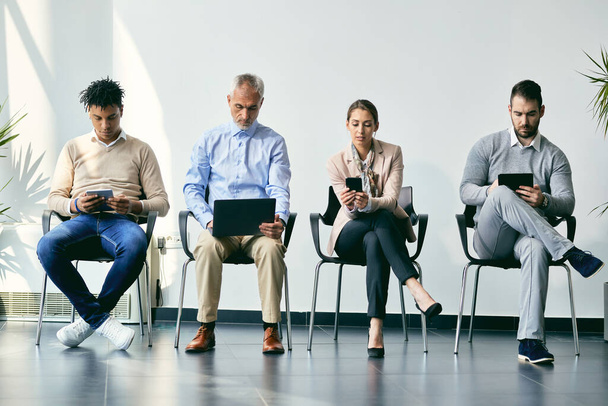 Small group of business people using wireless technology while anticipating job interview. - Photo, image