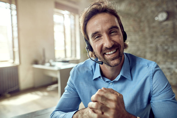 Young happy businessman wearing headset and looking at the camera while working in the office.  - Foto, immagini