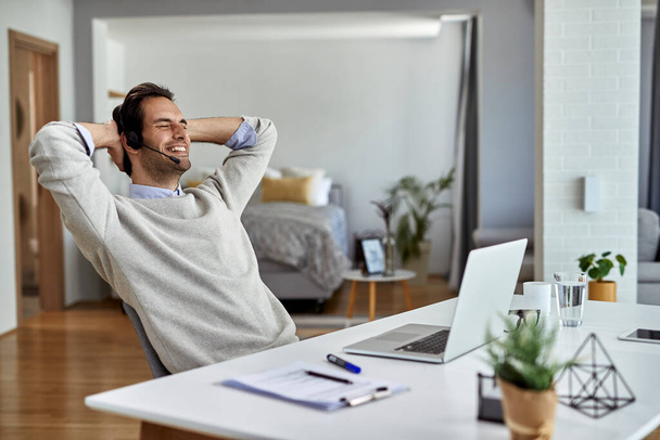 Young happy entrepreneur relaxing with hands behind head after working on a computer at home. - Foto, Bild