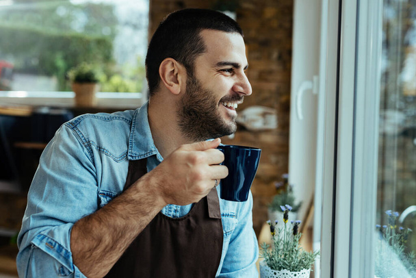 Молодий щасливий чоловік п'є каву і дивиться крізь вікно
.  - Фото, зображення