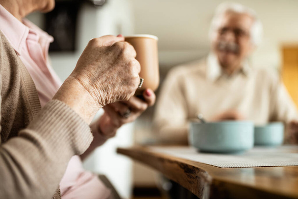 Крупним планом старша жінка п'є каву, снідаючи зі своїм чоловіком вдома
.   - Фото, зображення