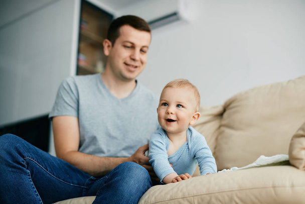 Cute baby boy crawling on the sofa while spending time with his father at home. - Photo, Image