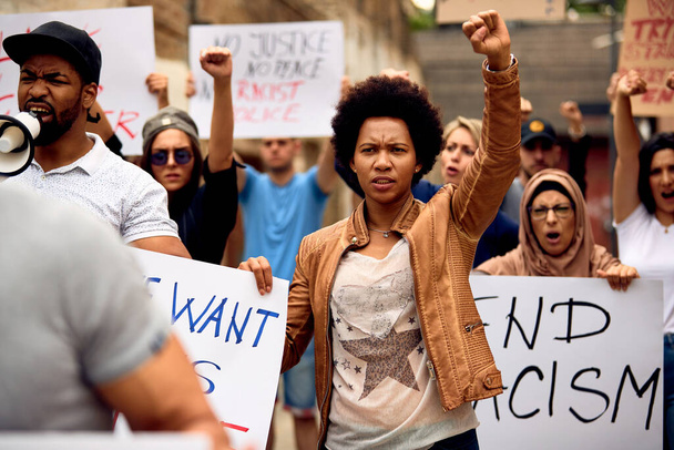 Multi-ethnic crowd of people protesting against racism on city streets. Focus is on African American woman with raised fist. - Foto, imagen