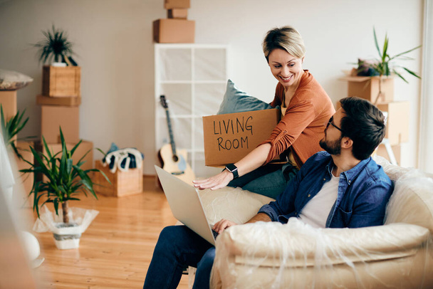 Щаслива жінка і її чоловік розмовляють, використовуючи ноутбук у своїй новій квартирі
.  - Фото, зображення