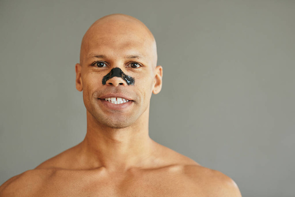Smiling mixed race man purifying his skin with charcoal cleansing nose strips and looking at camera. - Foto, Bild