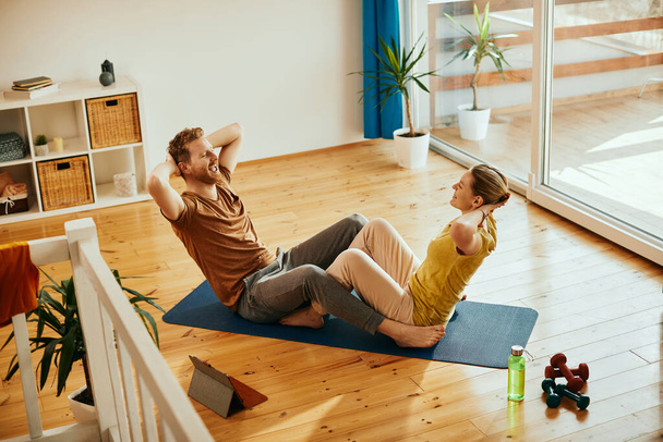 High angle view of happy couple cooperating while doing sit-up and exercising at home.  - Foto, Imagem