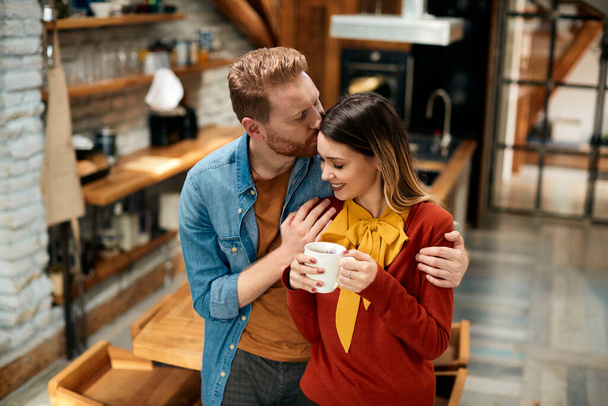 Young woman being kissed by her boyfriend while having cup of coffee at home.  - Foto, Imagem