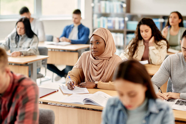 Female African American student in hijab writing during a class at university classroom. - Valokuva, kuva