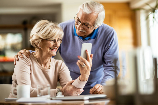 Happy mature couple using smart phone at home.  - Φωτογραφία, εικόνα