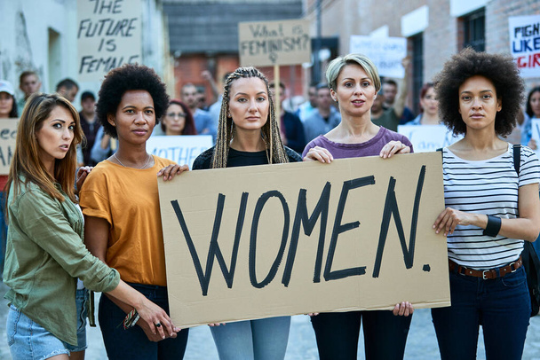 Group of females holding a banner with inscription 'women' while participating in street demonstrations.  - Foto, afbeelding