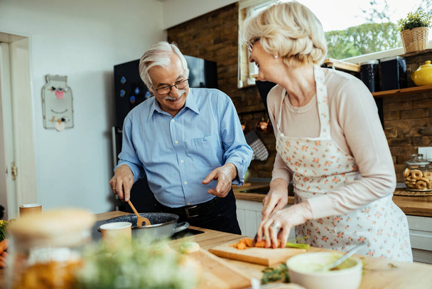 Щаслива старша пара розмовляє і розважається під час приготування їжі на кухні
.  - Фото, зображення