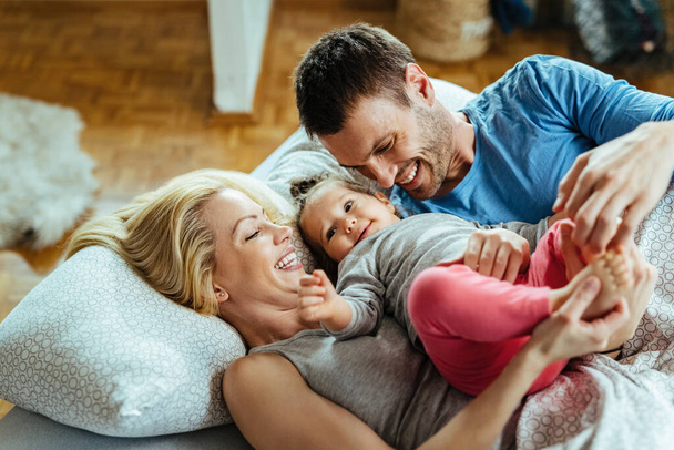 Young happy parents having fun with their small daughter while relaxing on the bed.  - 写真・画像