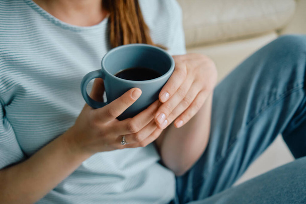 Unrecognizable woman drinking coffee while relaxing on the sofa at home.  - Photo, Image
