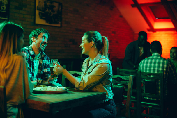 Young happy couple having fun and toasting with beer in a pub at night.  - 写真・画像