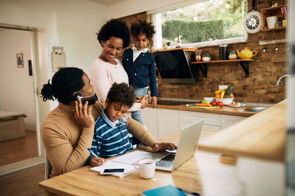 Щасливі чорні батьки з дитиною спілкуються вдома. Чоловік працює на ноутбуці
. - Фото, зображення