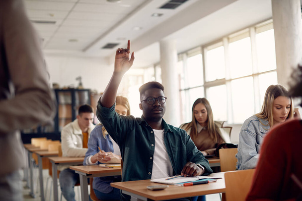 Black university student raising his arm to answer a question while having class in the classroom. - 写真・画像