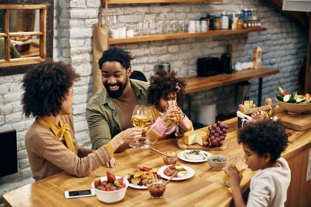 Happy black parents toasting with wineglasses while sitting with their kids at dining table.  - Φωτογραφία, εικόνα