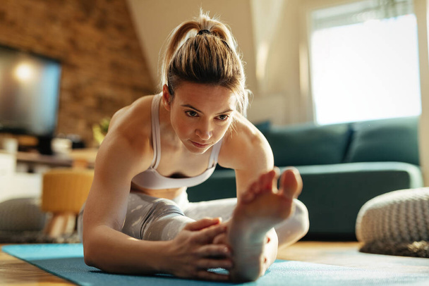 Jonge atletische vrouw doet stretching oefeningen op de vloer thuis.  - Foto, afbeelding