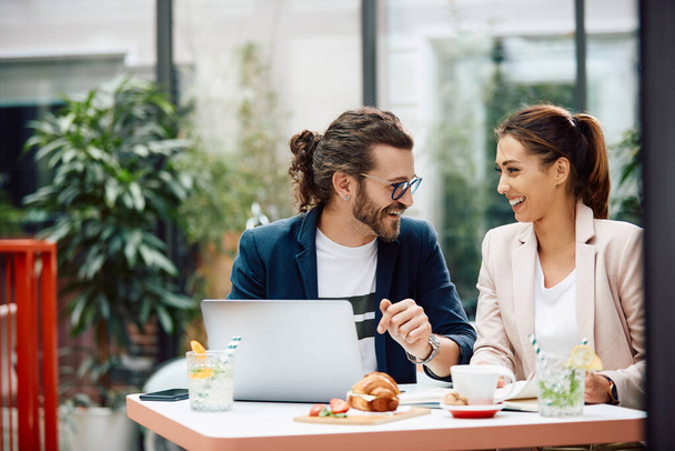 Ευτυχισμένος επιχειρηματίας και η γυναίκα συνάδελφός του επικοινωνούν ενώ εργάζονται σε υπολογιστή σε ένα καφέ. - Φωτογραφία, εικόνα