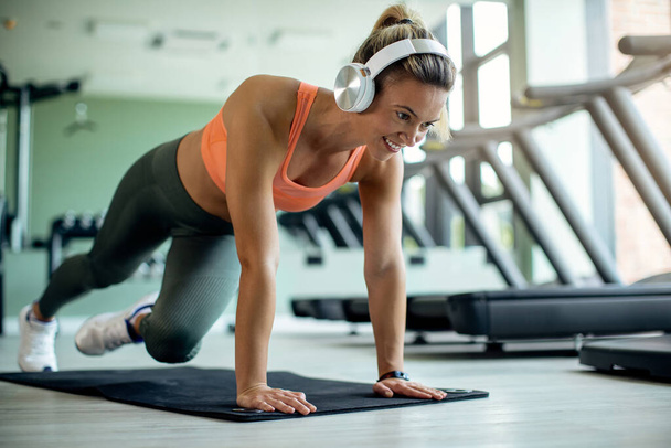 Happy athletic woman wearing headphones while exercising on the floor at health club.  - Foto, immagini