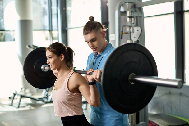 Young sportswoman lifting barbell while having weight training with her coach in a gym.  - Fotoğraf, Görsel