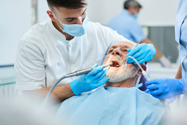 Young dentist using dental polish on senior man's teeth during dental procedure at dentist's office.   - Photo, image