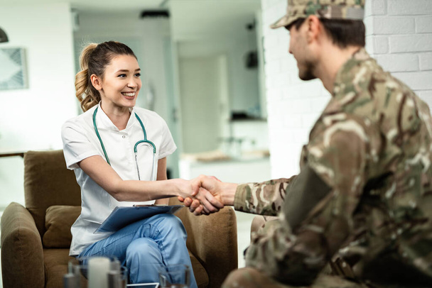 Happy female doctor and military man shaking hands while meeting at his home.  - Foto, Imagen