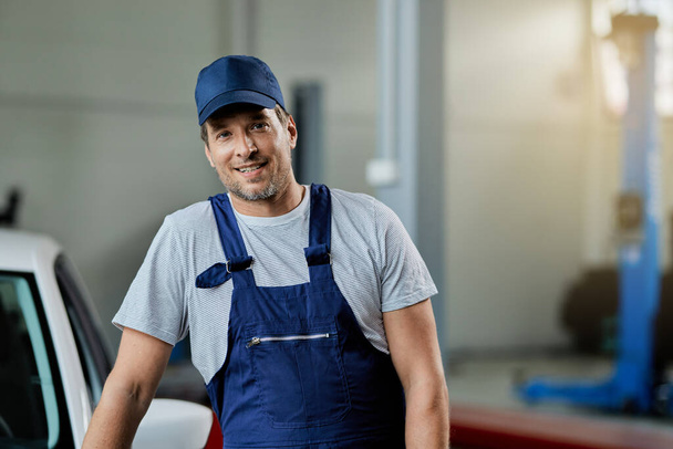 Porträt eines lächelnden Automechanikers, der in der Autowerkstatt steht und in die Kamera blickt. - Foto, Bild