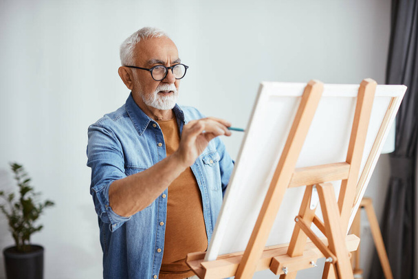 Mature man creating a new painting on canvas at home. - Fotografie, Obrázek